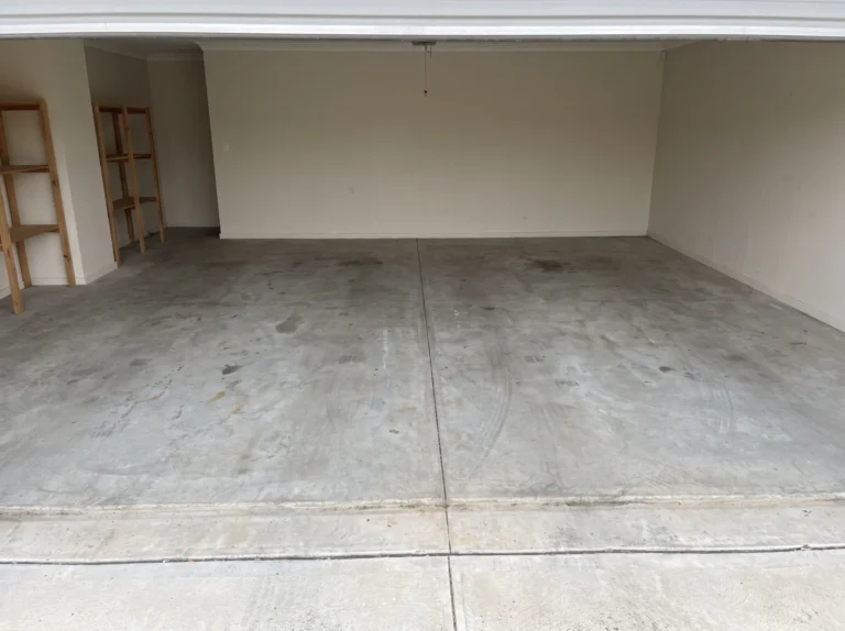 Empty double garage with a bare grey concrete floor photographed from the open doorway