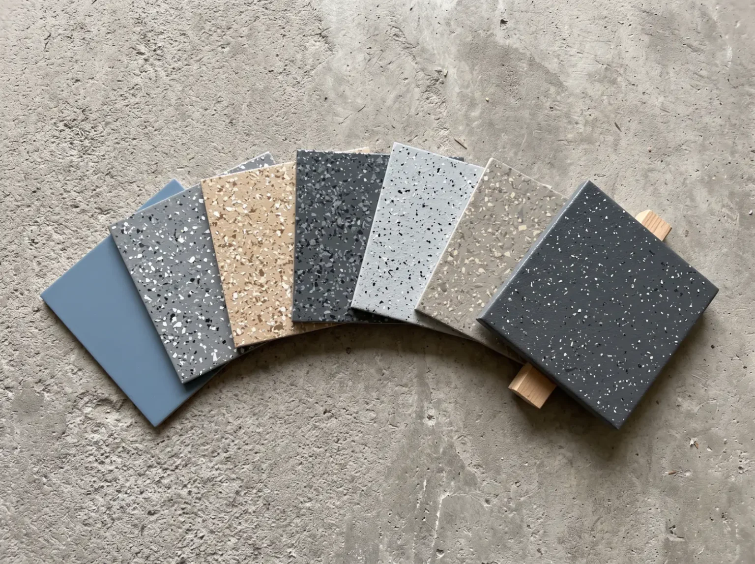 Flooring finish sample panels in flake and solid colour blends laid out on a bare concrete slab